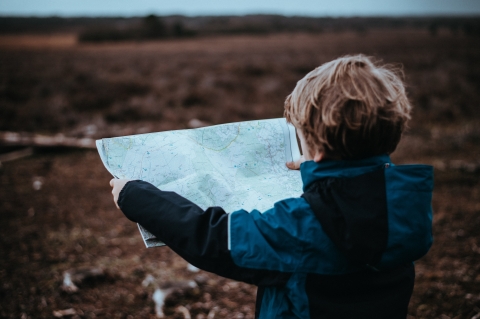 a young boy holds a map and looks to a fall horizon